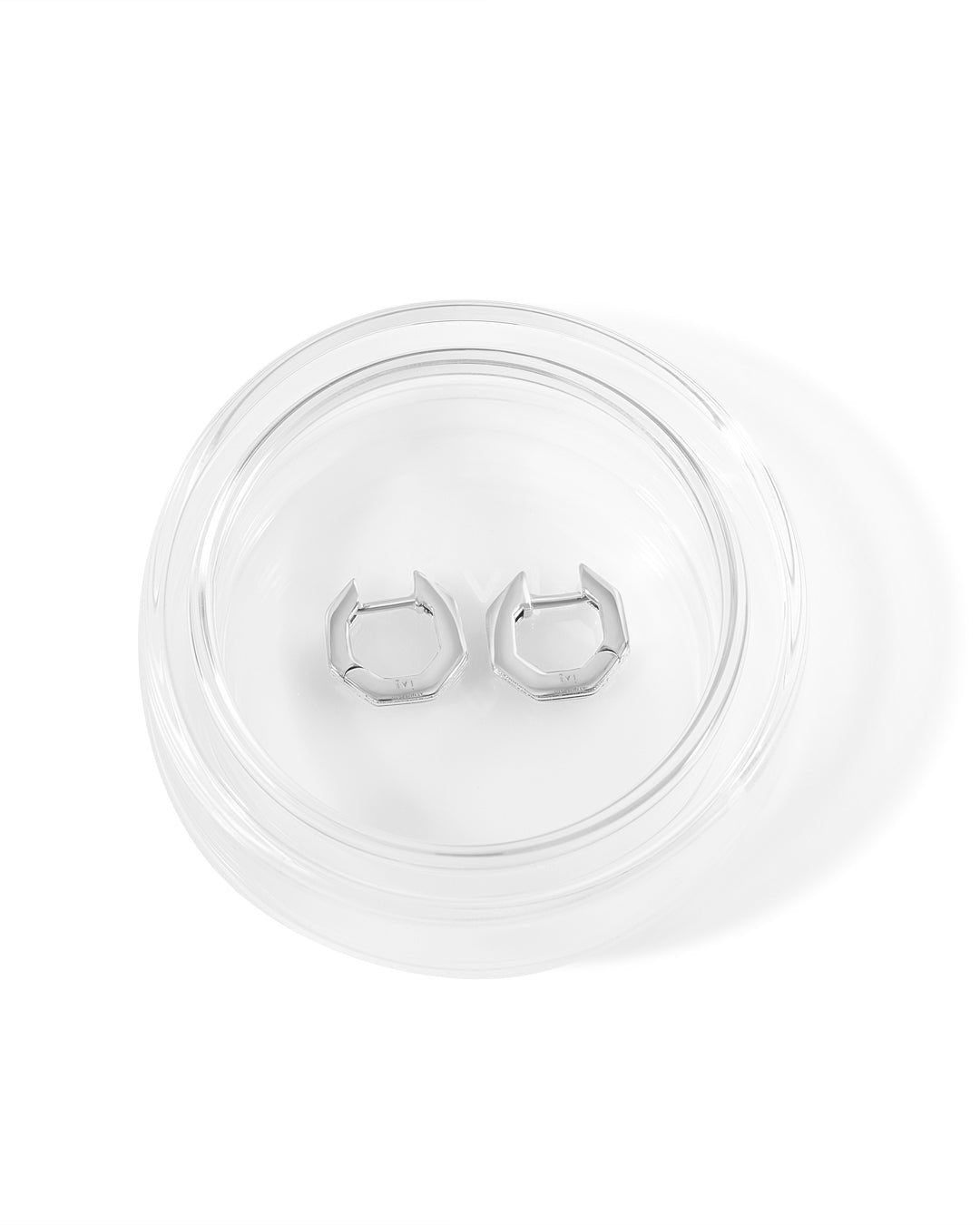 Silver huggies earrings on a clear display stand against a white background
