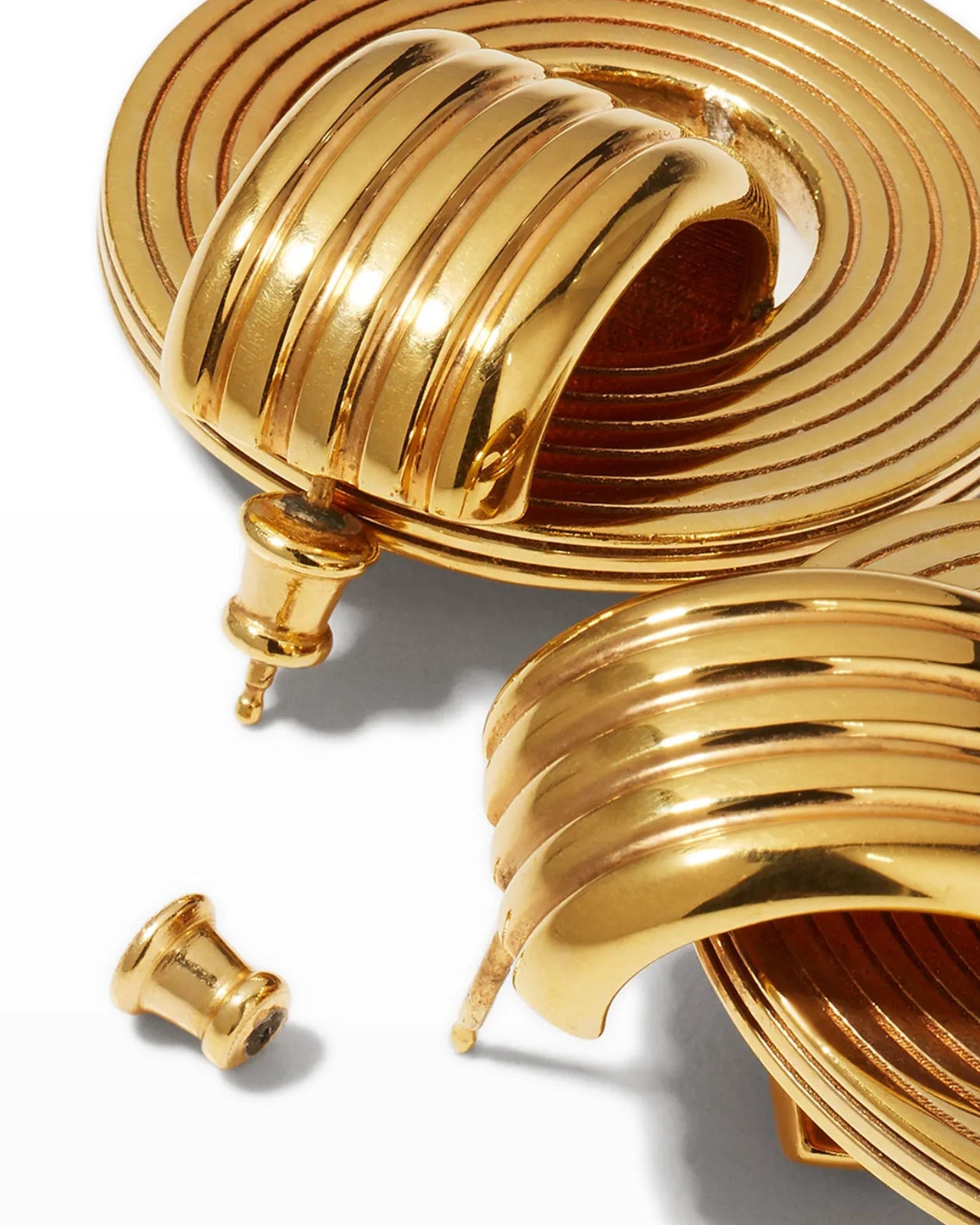 A close up of a pair of gold-plated oval hoop earrings with a circular pendant attached to the hoop, featuring intricate engravings.