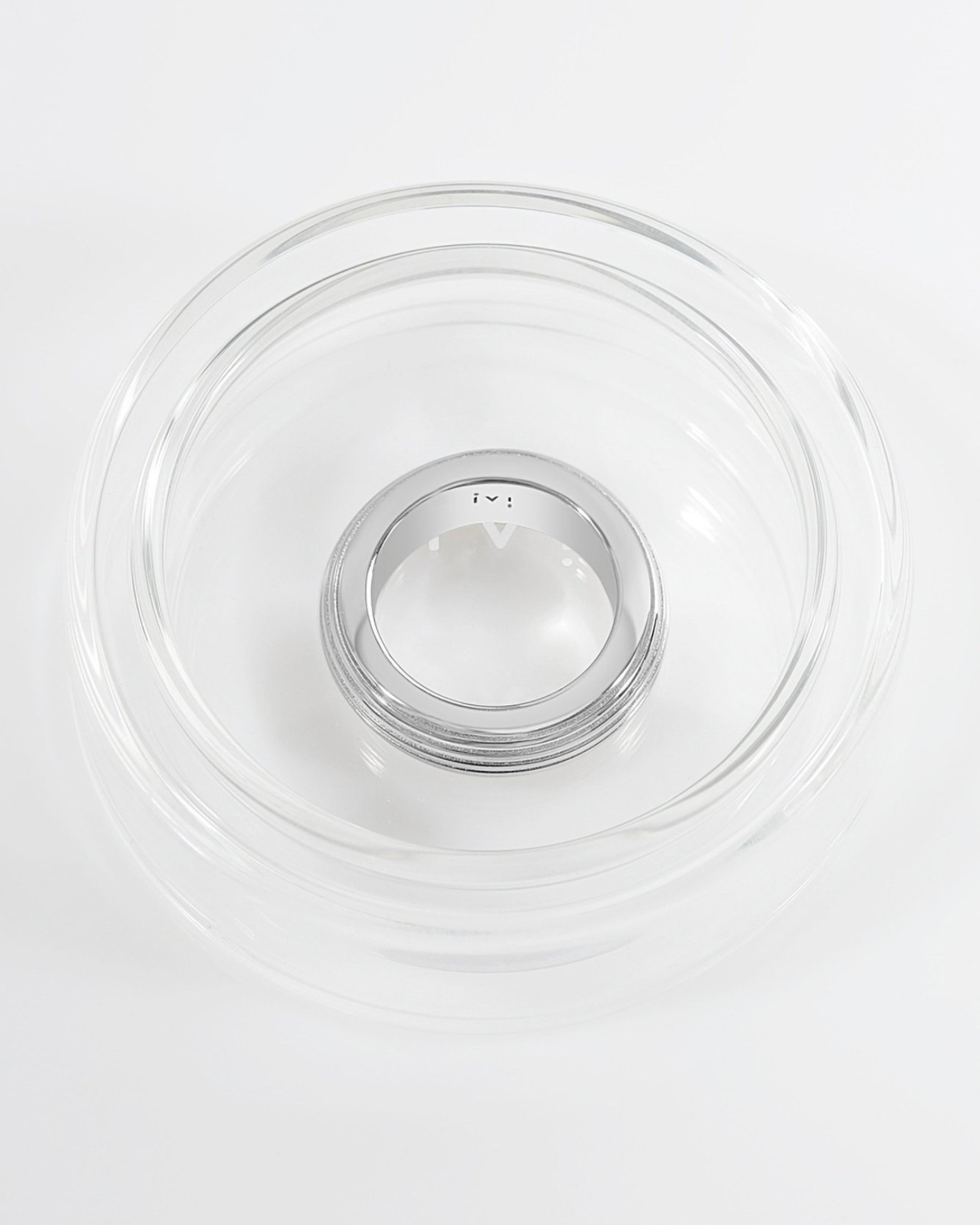 A rhodium-plated, round-shaped ring with linear engravings placed in glass packaging.