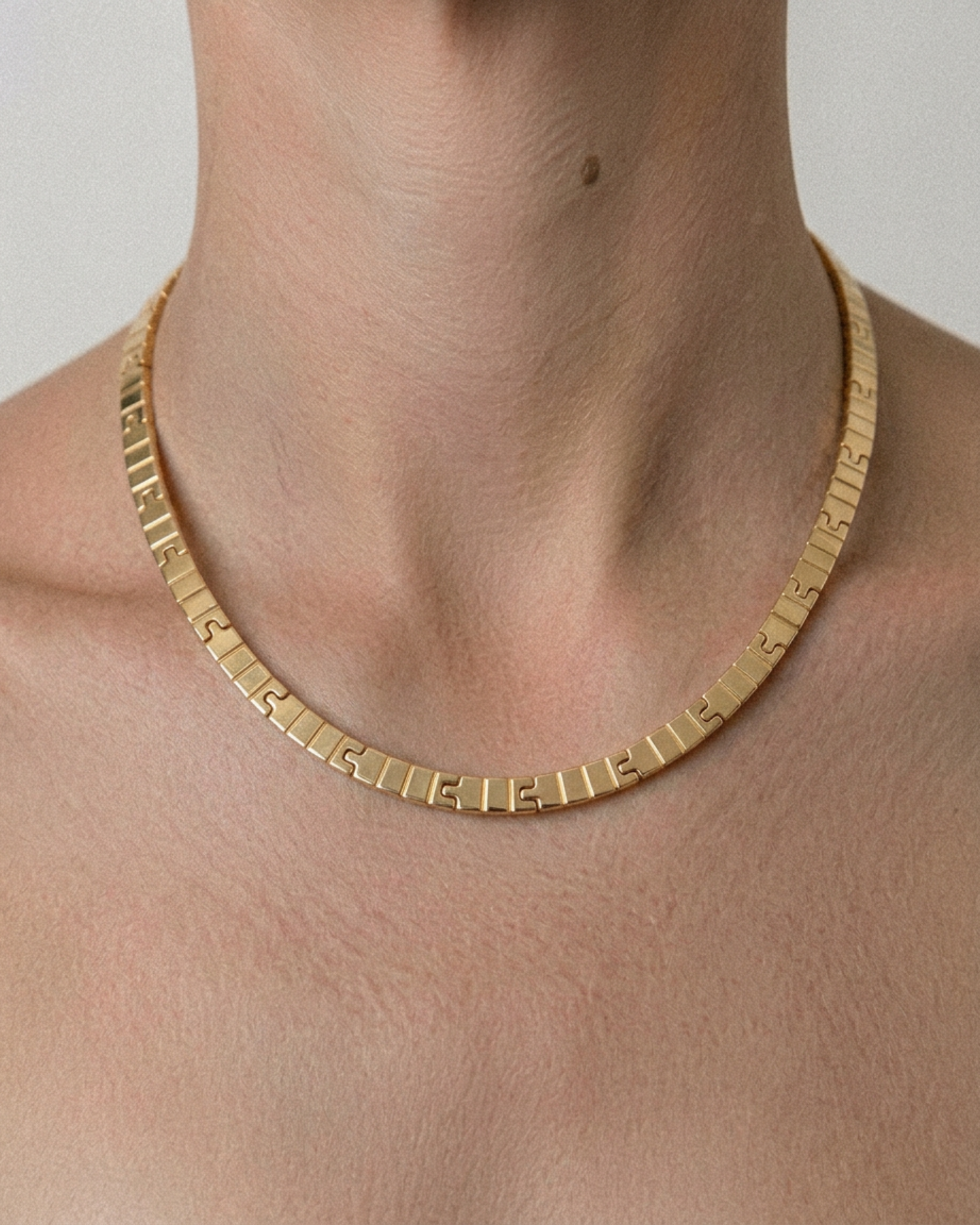Gold necklace on a person's neck against a neutral background