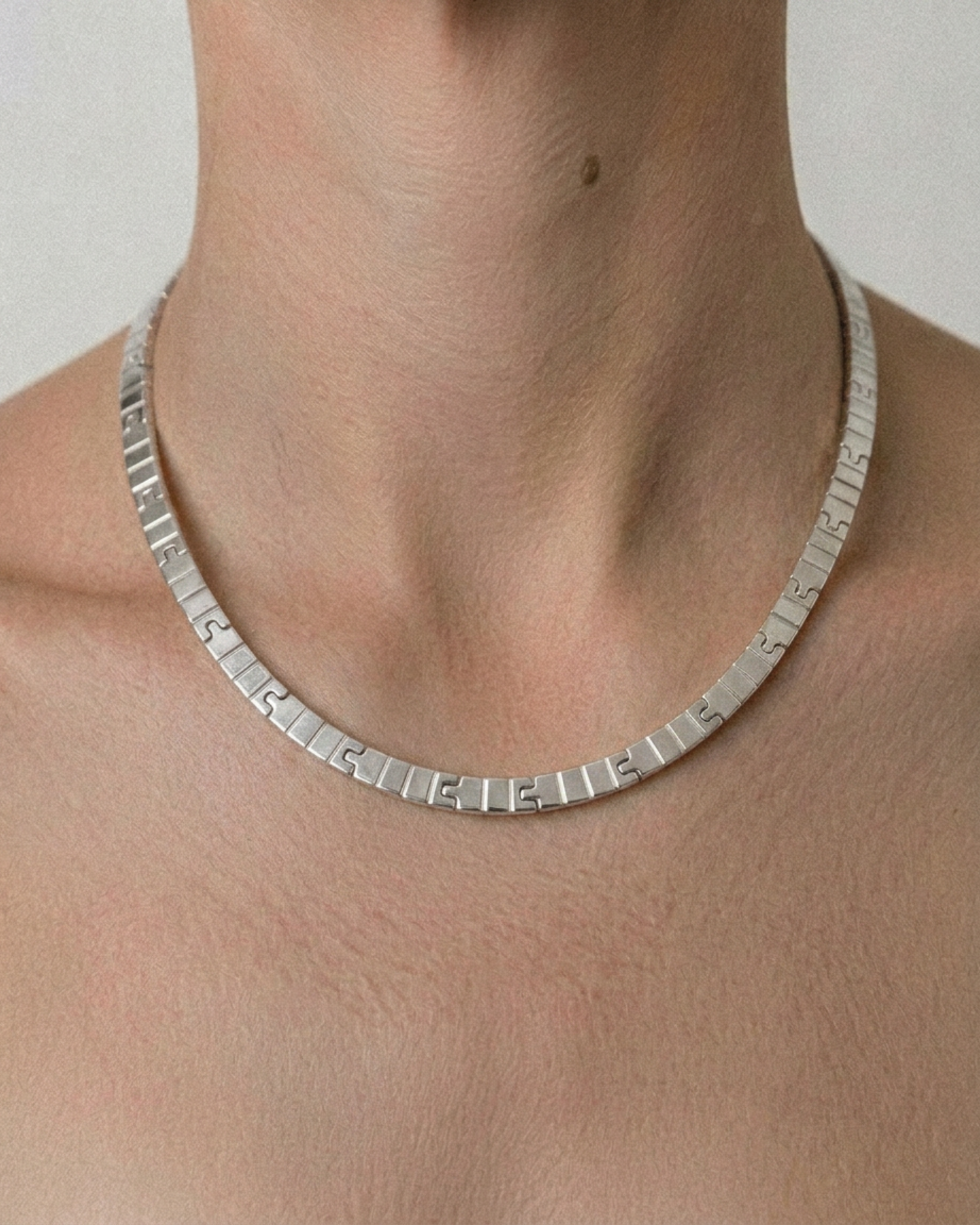Silver necklace on a person's neck against a neutral background
