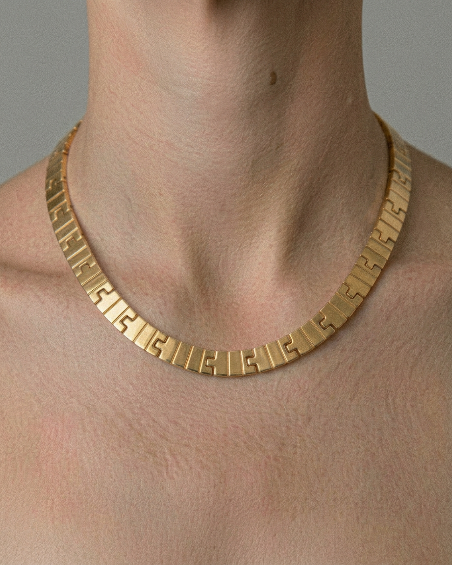 Gold necklace on a person's neck against a neutral background