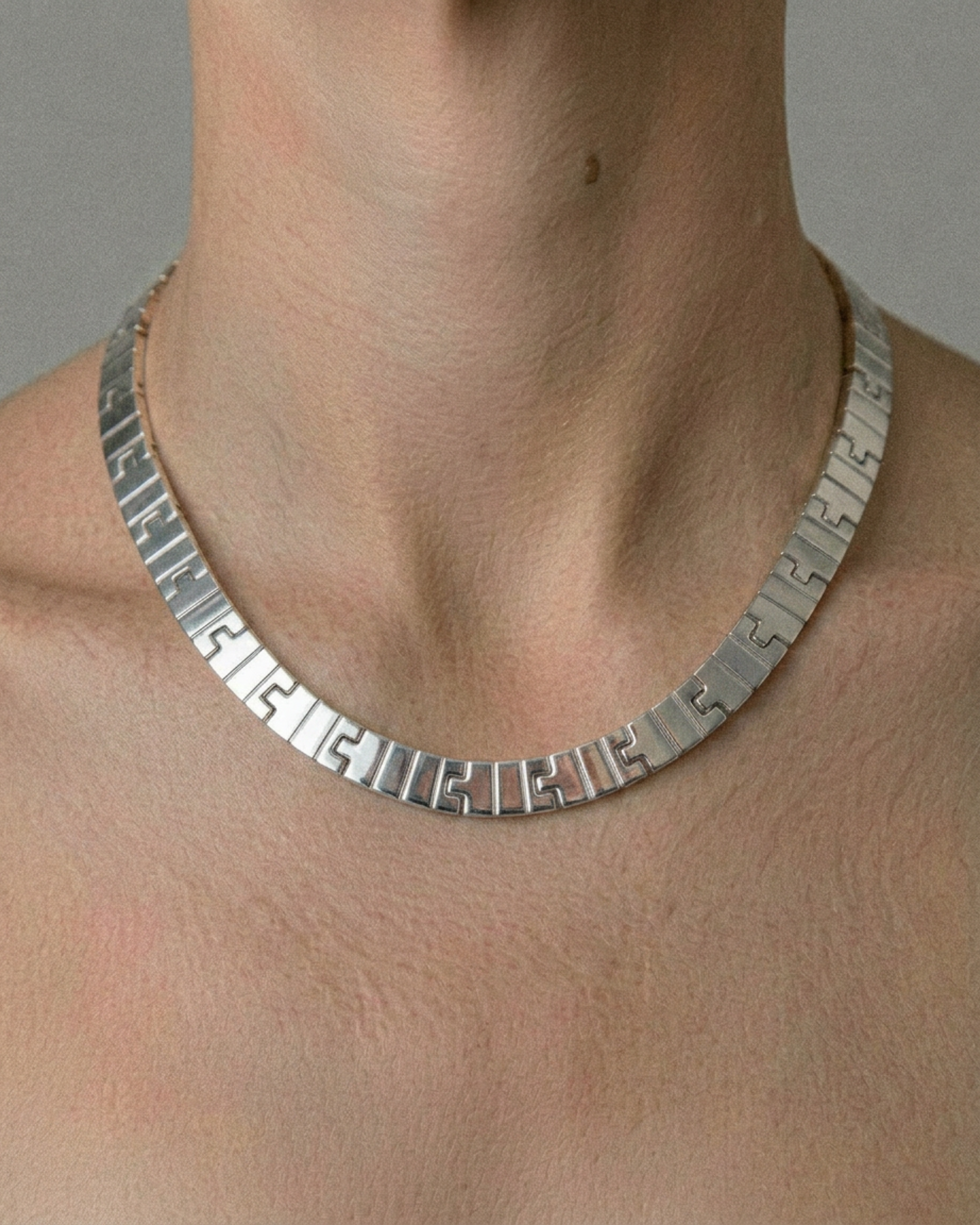 Silver necklace on a person's neck against a neutral background
