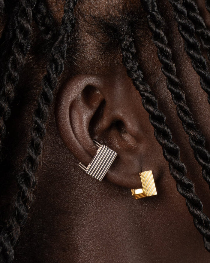 Pair of gold-plated Mini Aurelia sculptural square huggies on a white background worn by a model. 