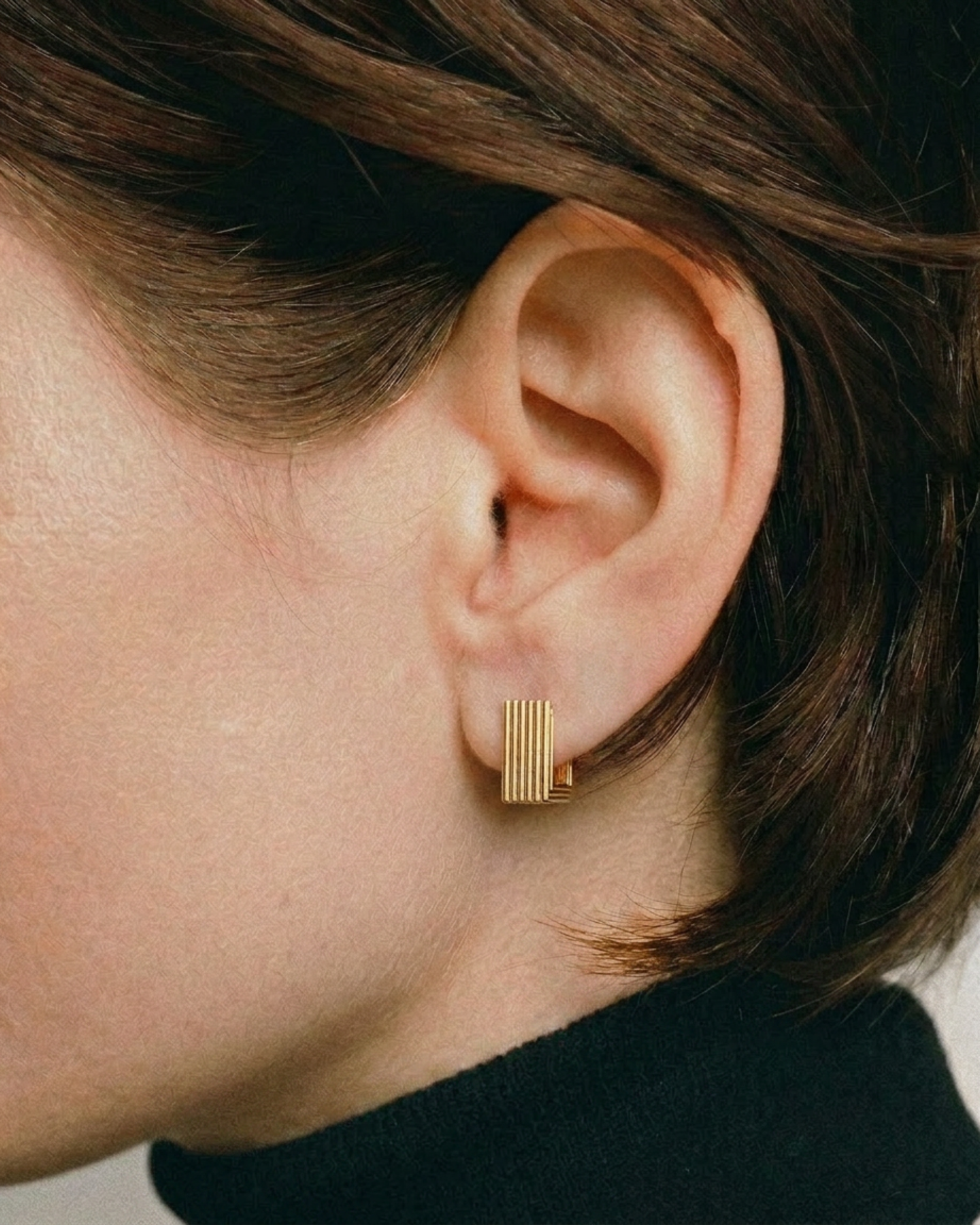 Gold earring worn by a person with short brown hair.