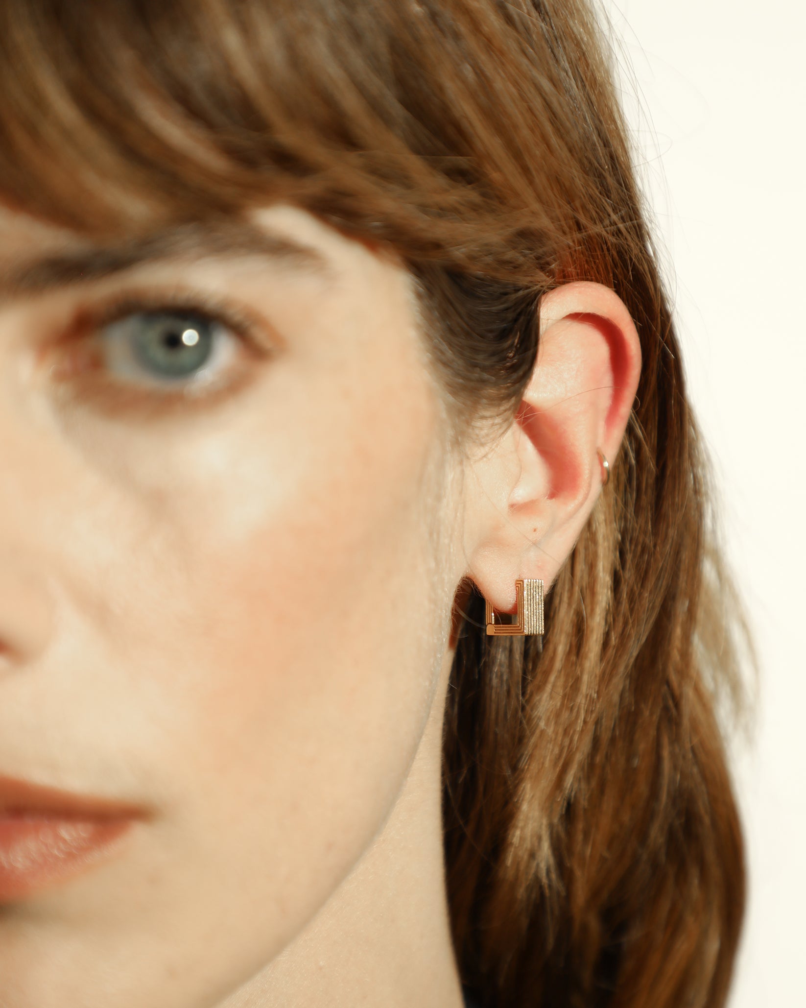 Pair of gold-plated Mini Aurelia sculptural square huggies worn by a model. 
