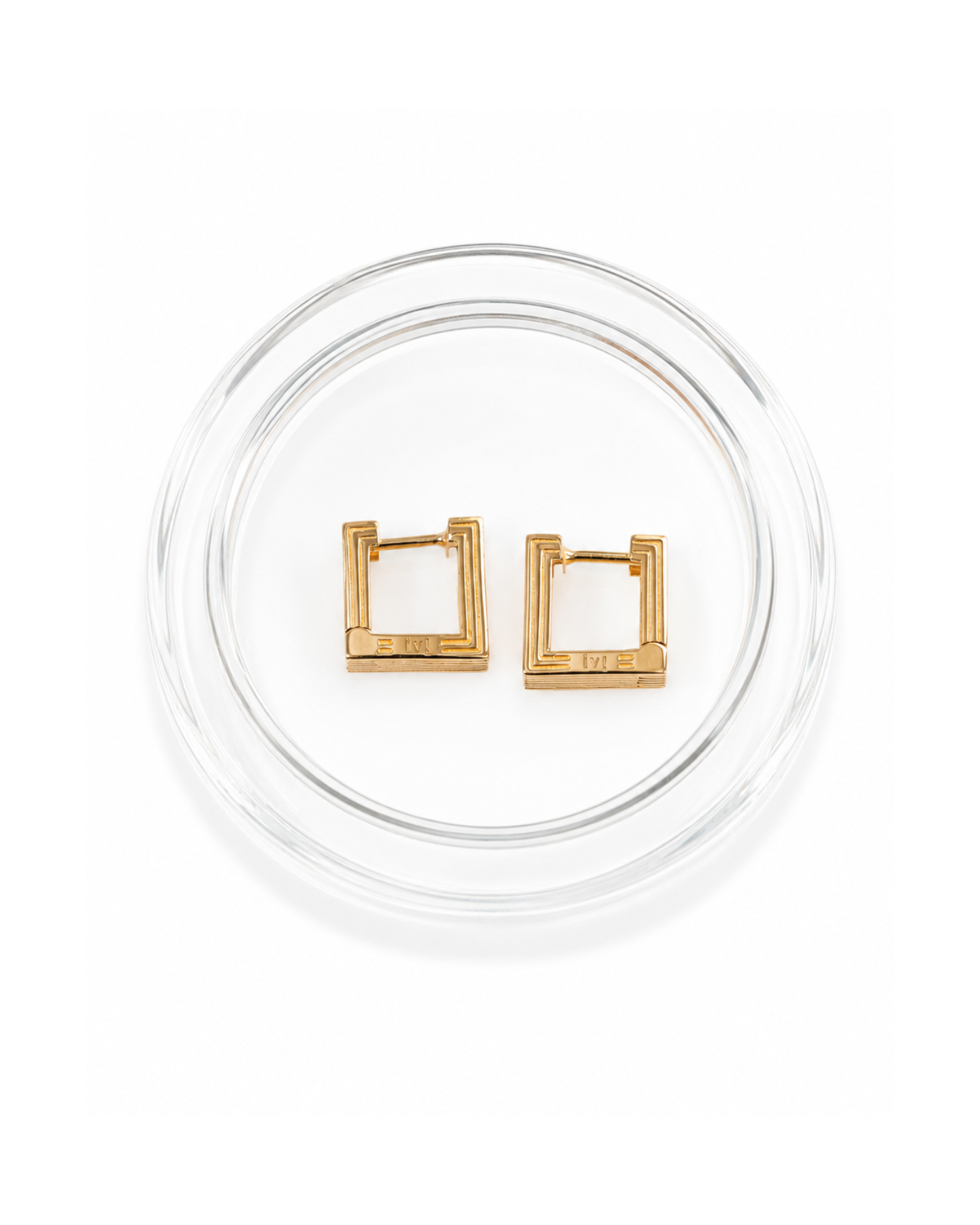 Gold square hoop earrings on a clear circular stand against a white background
