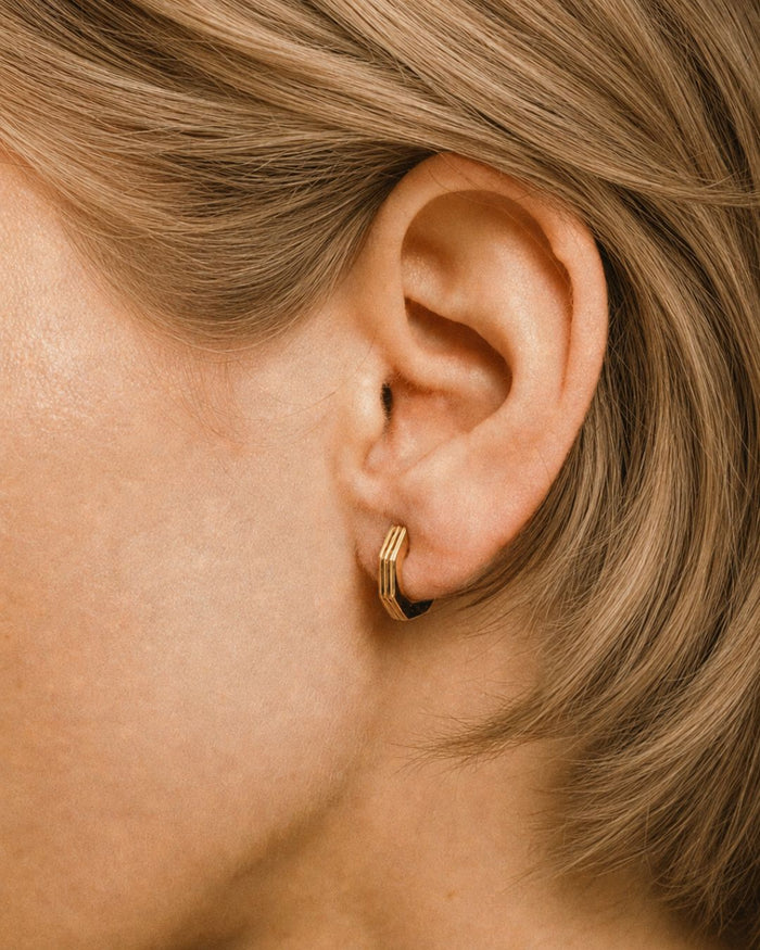 Close-up of an ear wearing a gold hoop earring with blonde hair.