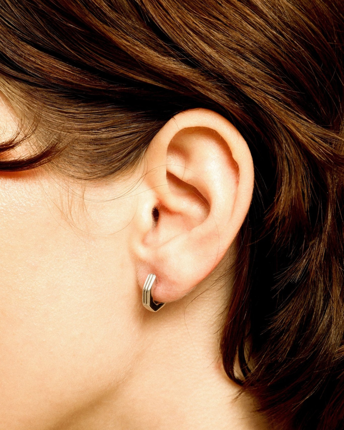Close-up of an ear wearing a silver hoop earring with brown hair.