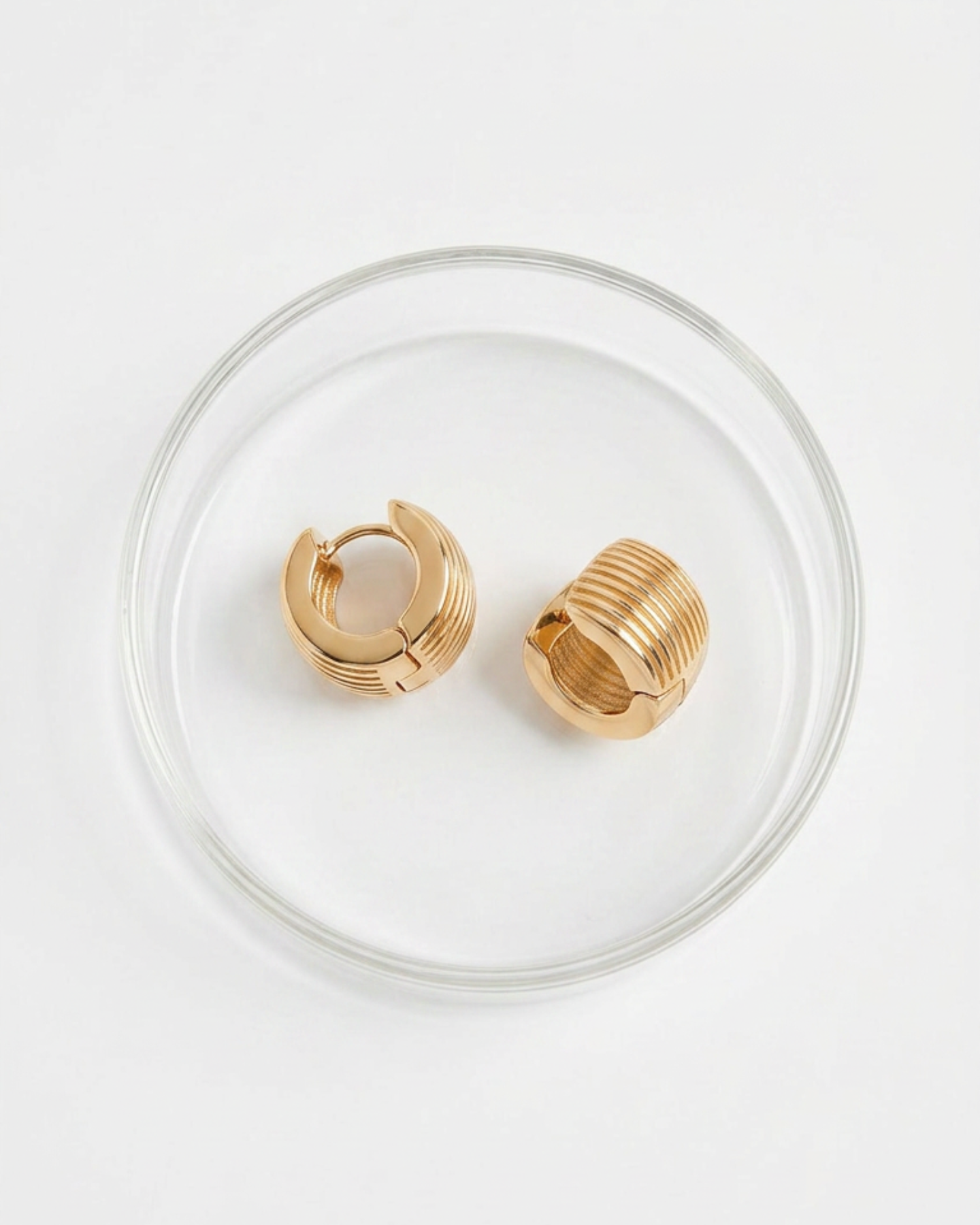 Gold hoop earrings on a clear glass dish with a white background