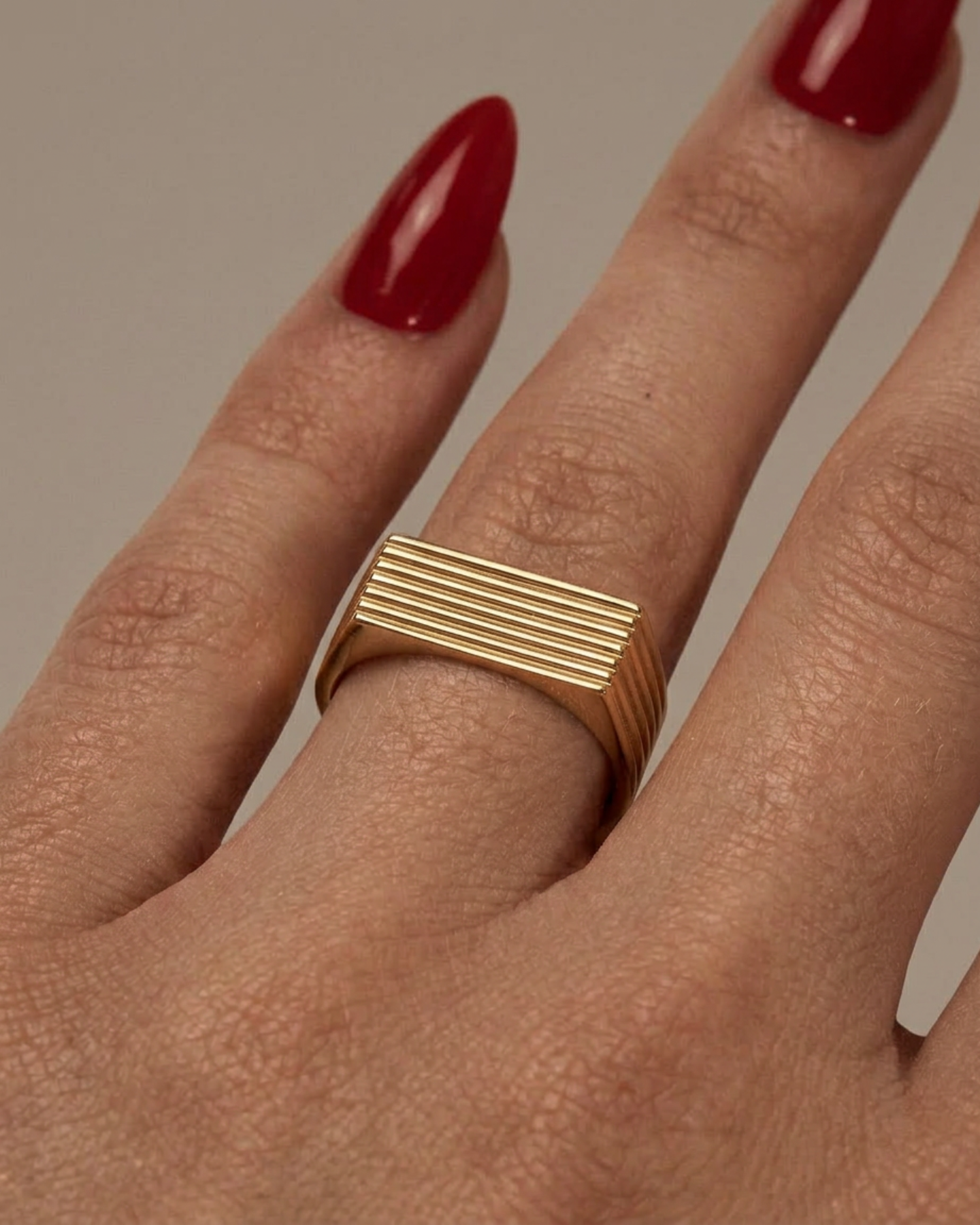 Gold ring on a finger with red nail polish against a neutral background
