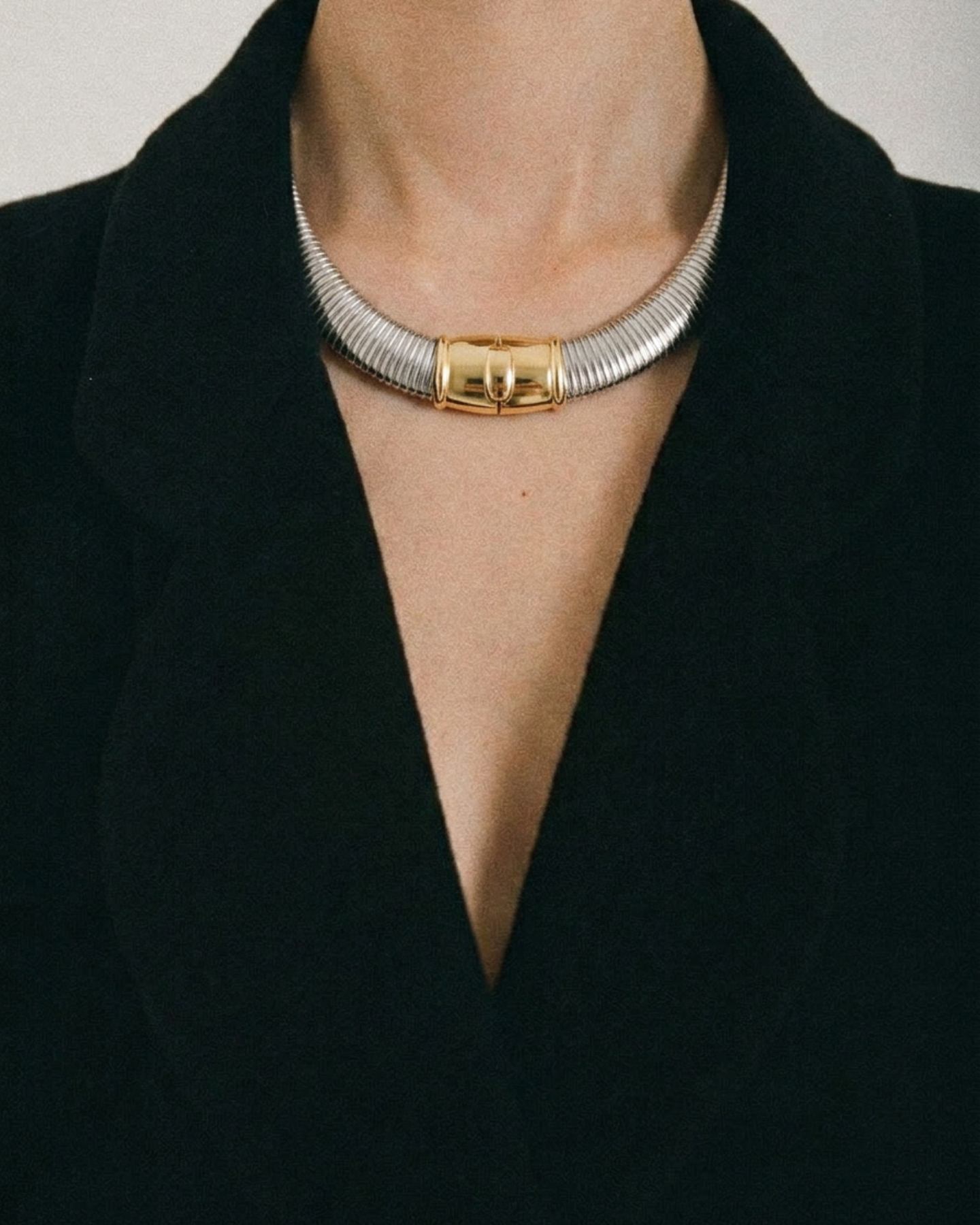 Gold and silver choker necklace on a person wearing a black outfit.