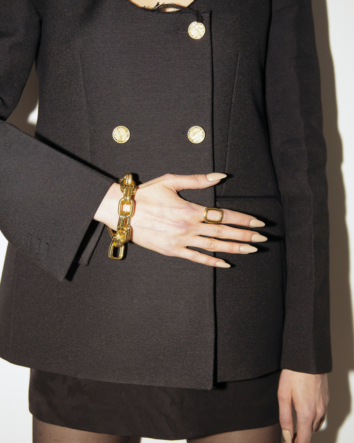 Person wearing a black coat with gold buttons, holding a gold bracelet.