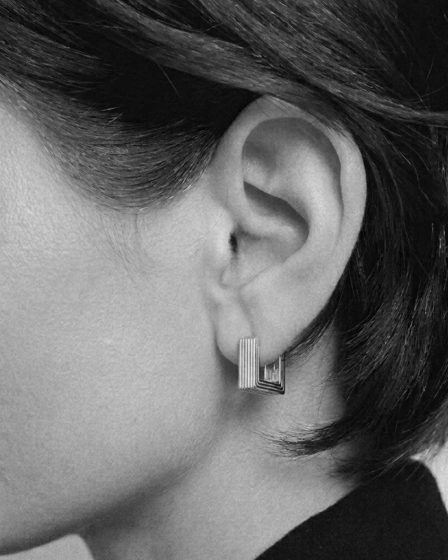 Close-up of an ear wearing a geometric earring with a blurred background