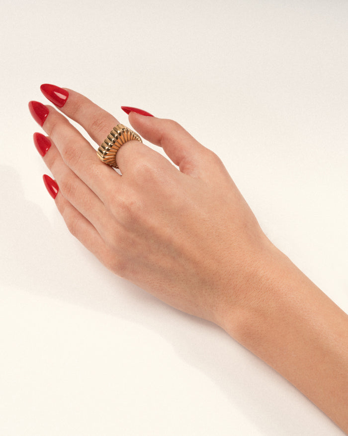 Bold gold ridged statement ring worn on a hand with red nails, shown in a lifestyle close-up.
