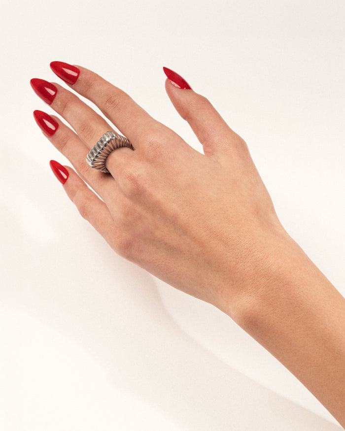 Bold silver ridged statement ring worn on a hand with red nails, shown in a lifestyle close-up.
