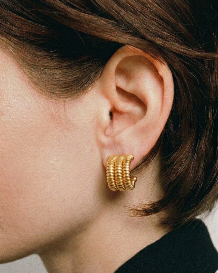 Gold hoop earrings worn by a person with short brown hair.