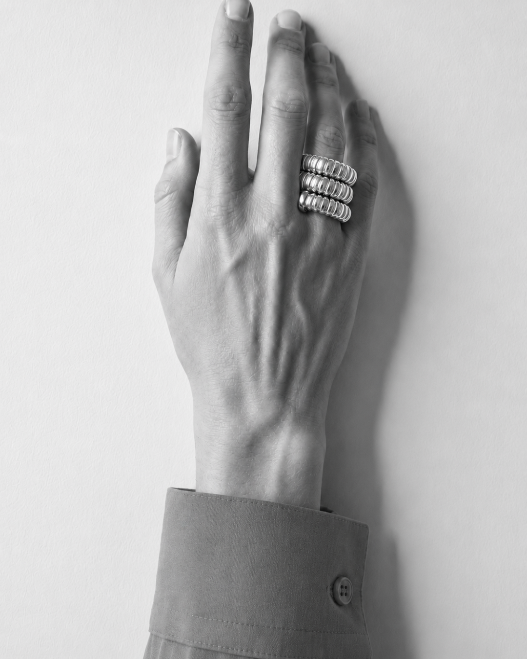 Hand wearing a gold-plated Gaia Triple Twist ring on a plain background