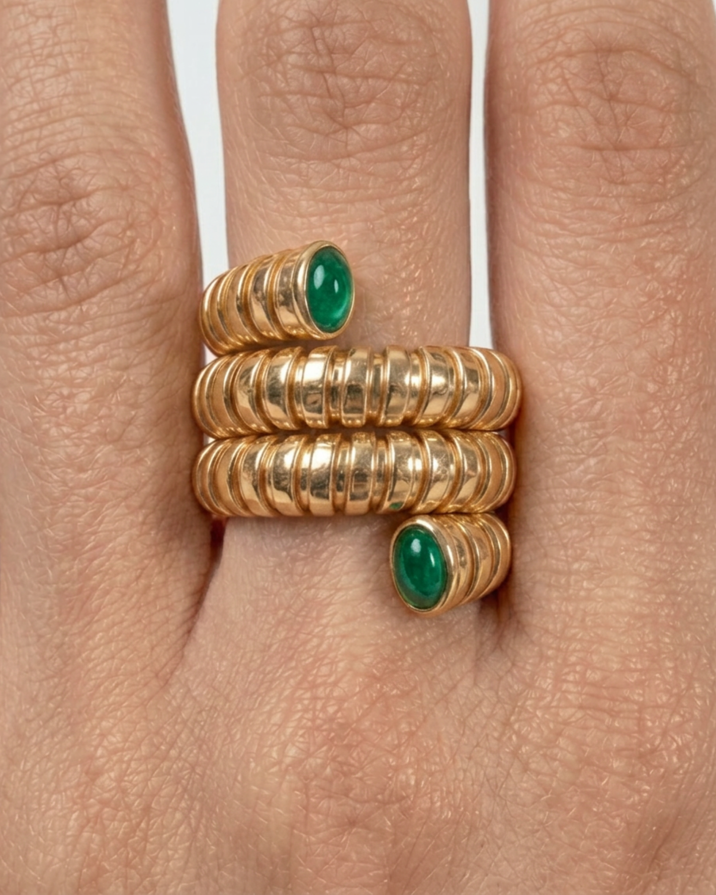 Gold rings with green gemstones on a finger against a neutral background