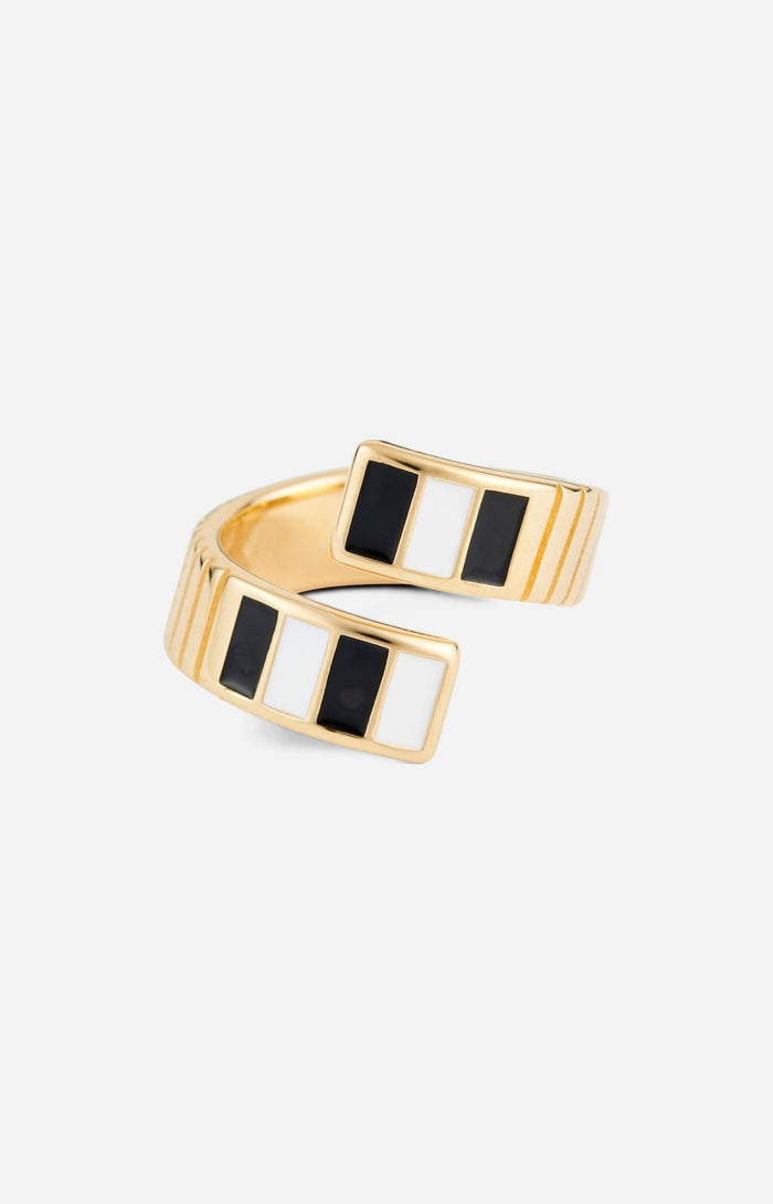 A gold-plated twist ring with polished black and white enamel stripes at the tips, with a textured surface and signature linear engravings.