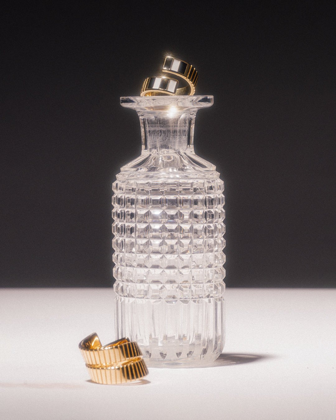 A gold-plated twist ring with polished black and white enamel stripes at the tips placed on a glass. 