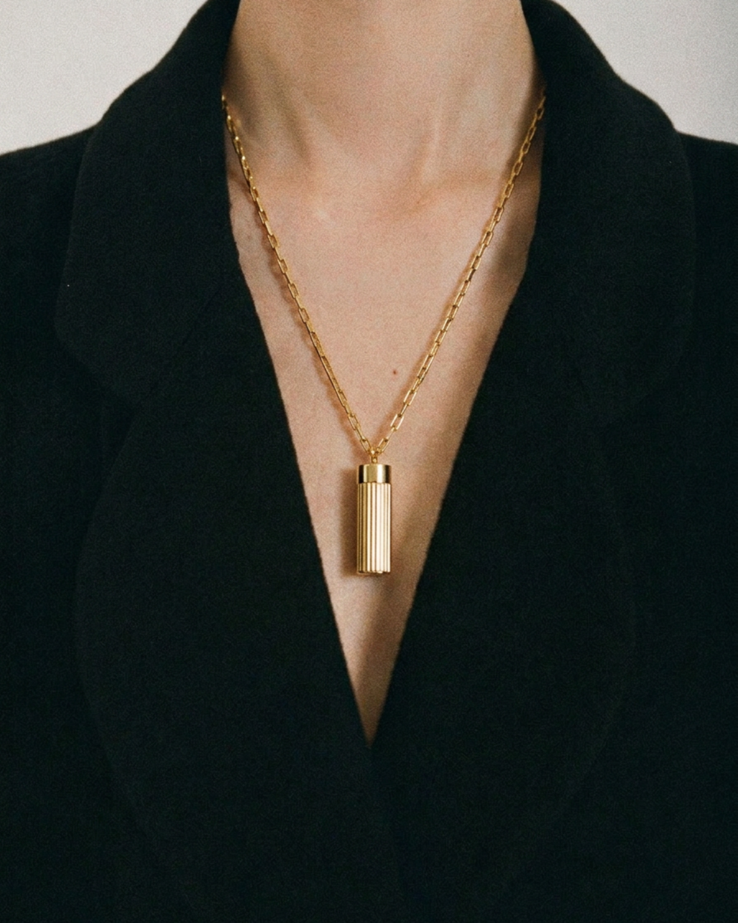 Gold necklace with a cylindrical pendant worn by a person against a black background