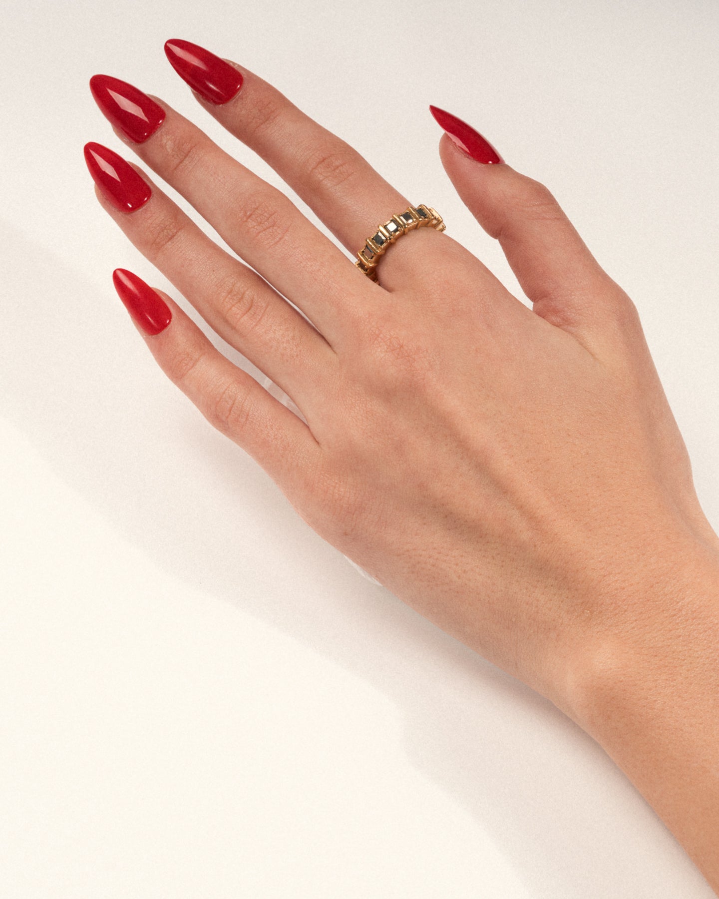 A gold-plated band ring with raised, squared frames set with shimmering pyrite stones worn on a hand with red nails, shown in a lifestyle close-up.