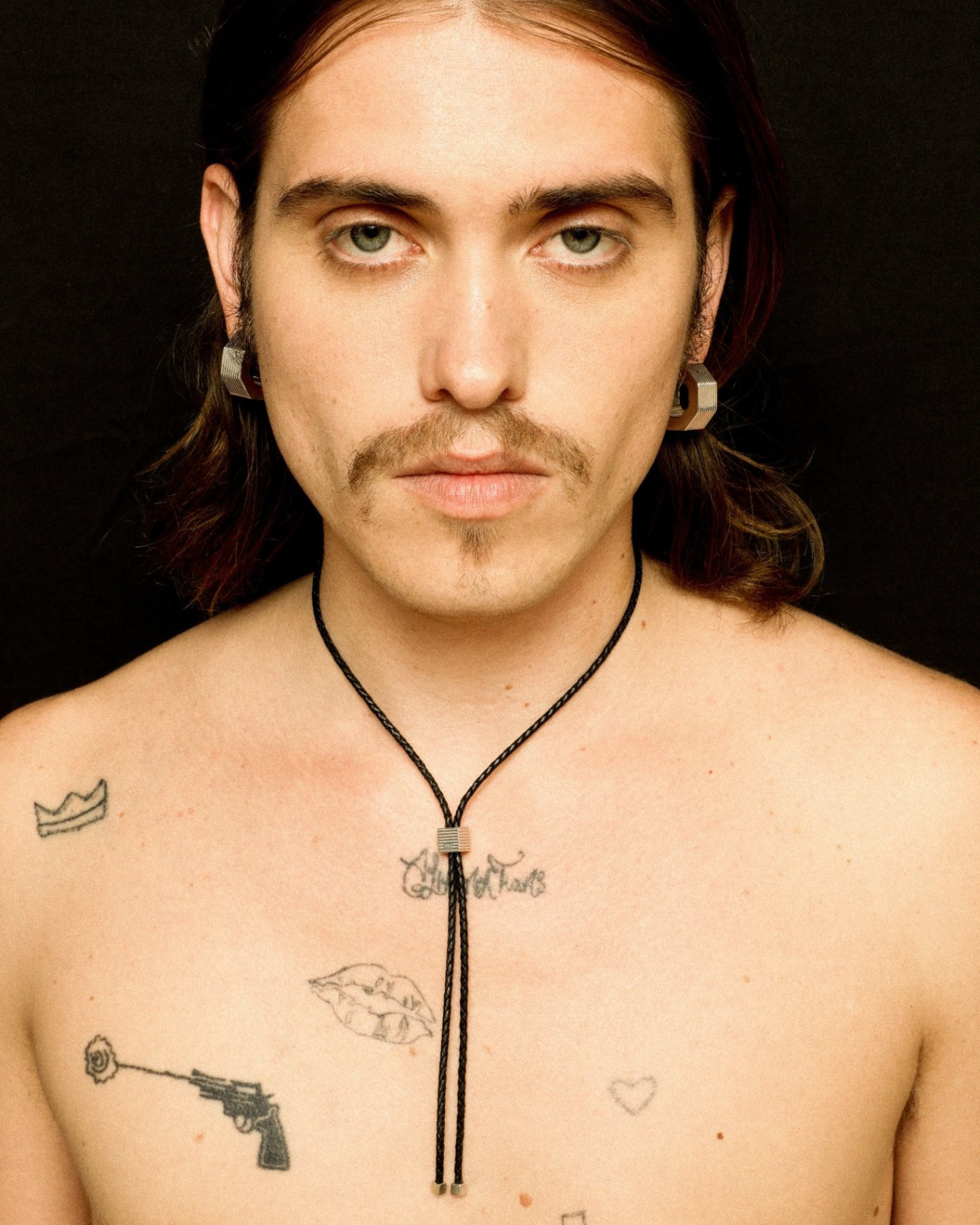 A bolo tie with an adjustable silhouette crafted from braided leather, with signature rhodium-plated cubes at the fastening and tips worn by a model.