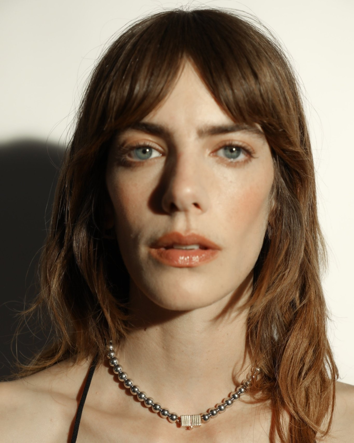 A silver necklace featuring a series of round rhodium-plated beads and a rectangular clasp with a small gold-tone detail worn by a model. 