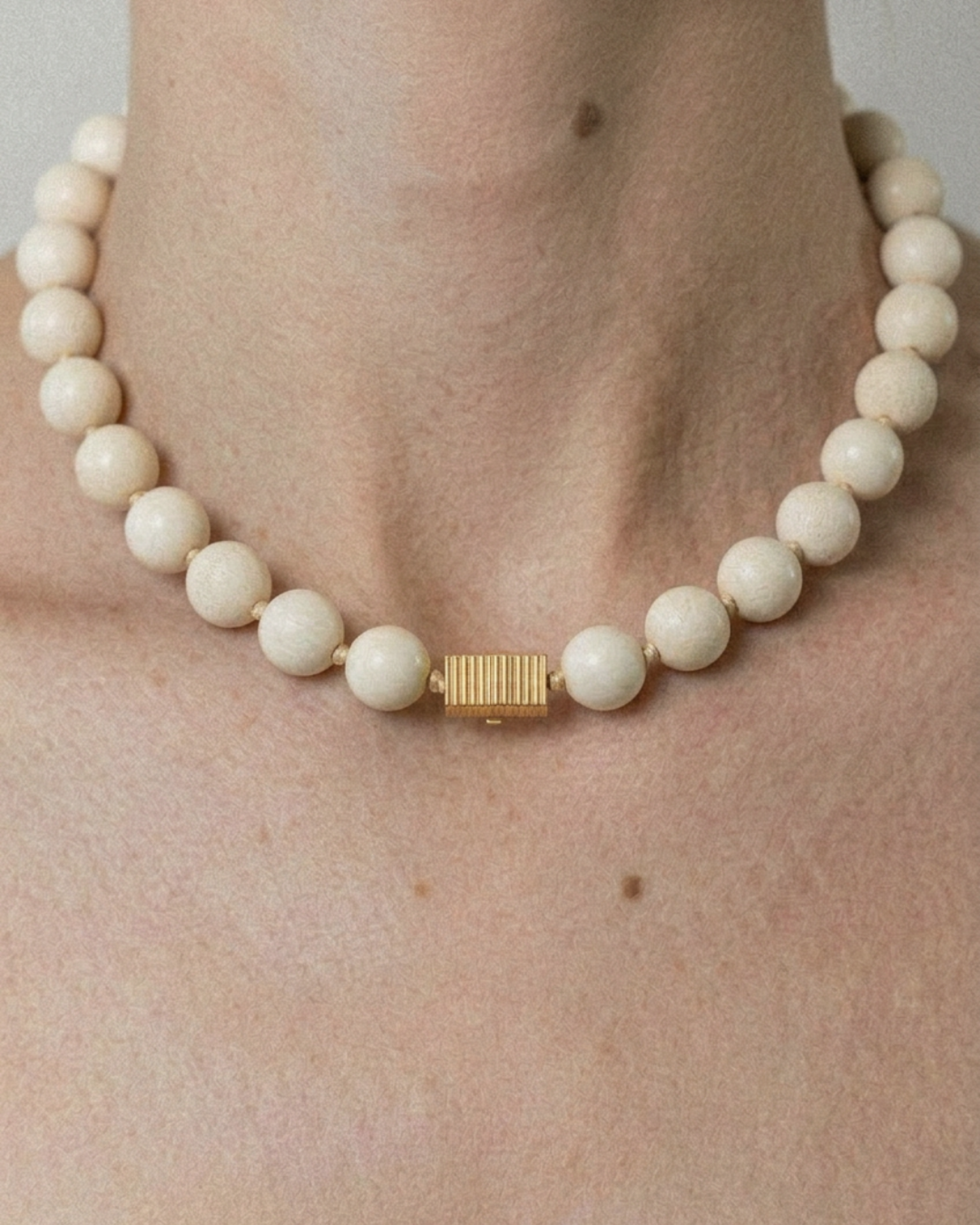White beaded necklace with a gold clasp on a person's neck against a neutral background