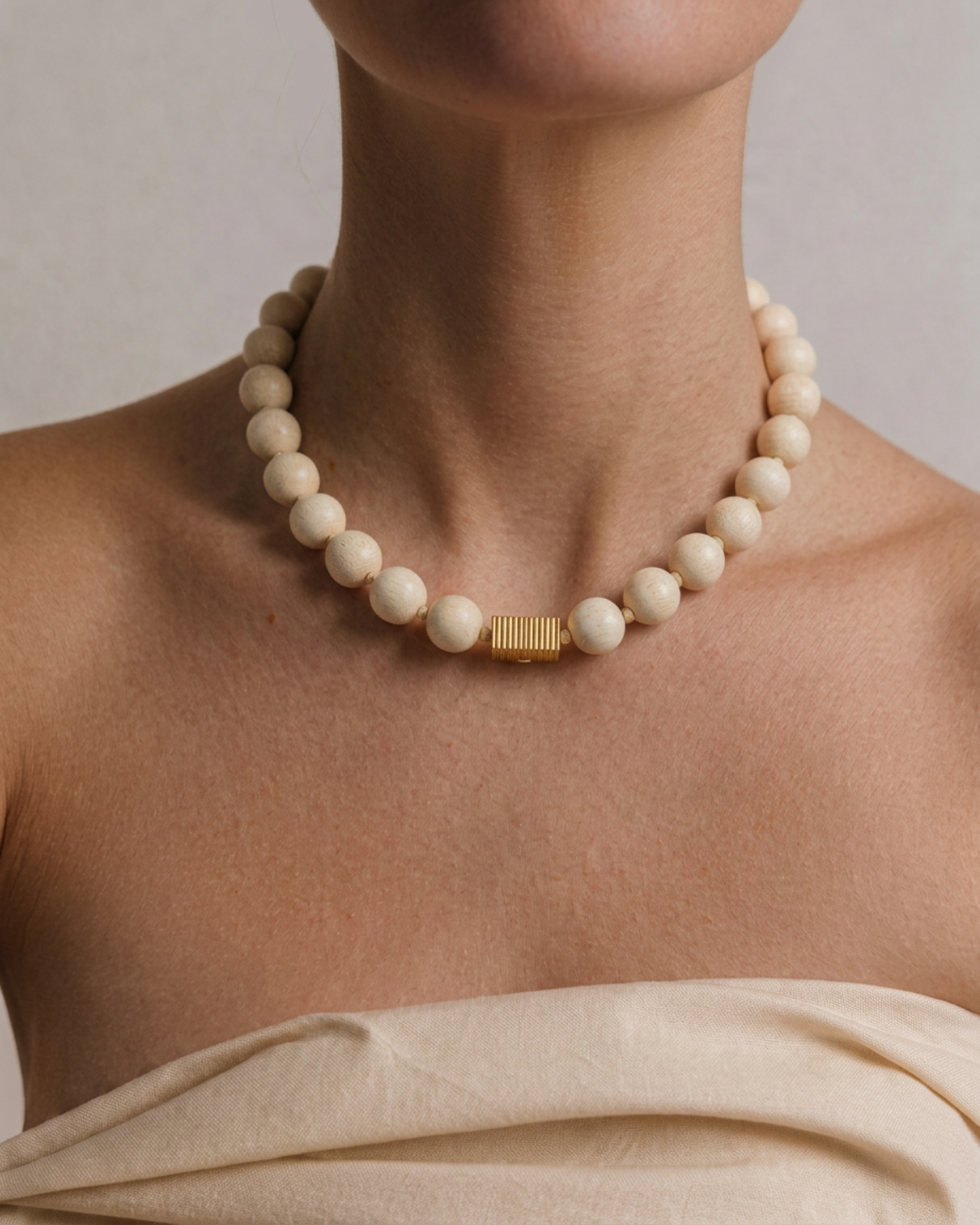 Necklace with white beads and gold clasp on a person wearing a beige top against a neutral background