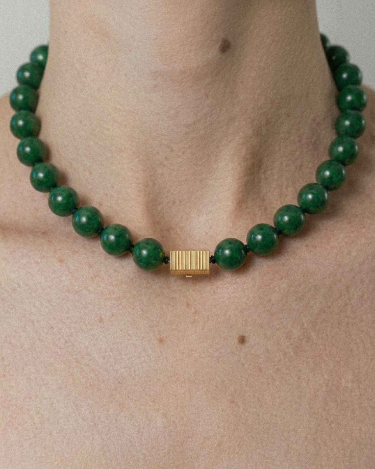 Green beaded necklace with a gold clasp on a person's neck against a neutral background