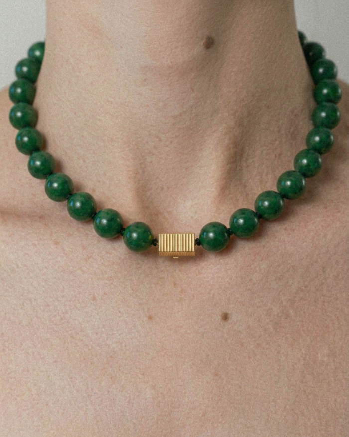 Green beaded necklace with a gold clasp on a person's neck against a neutral background