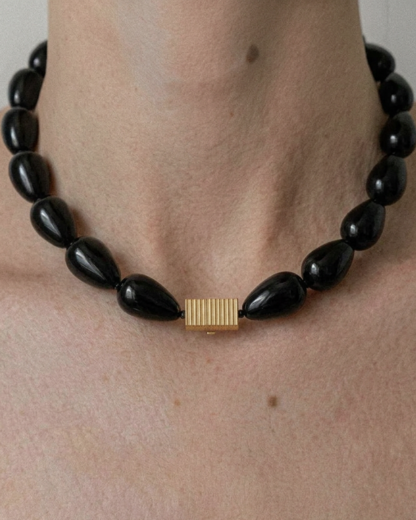 Black teardrop-shaped beaded necklace with a gold clasp on a person's neck
