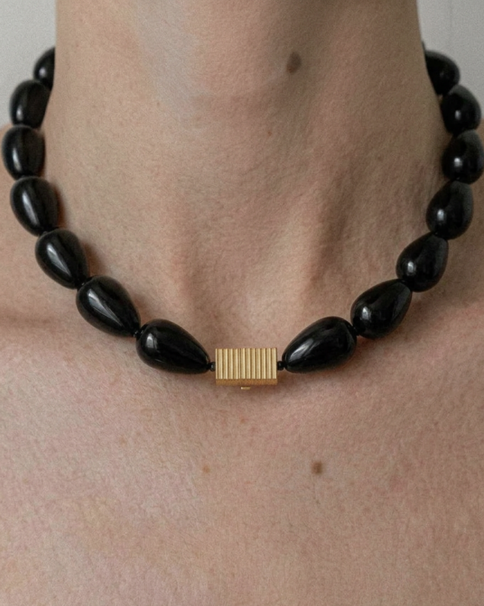 Black teardrop-shaped beaded necklace with a gold clasp on a person's neck