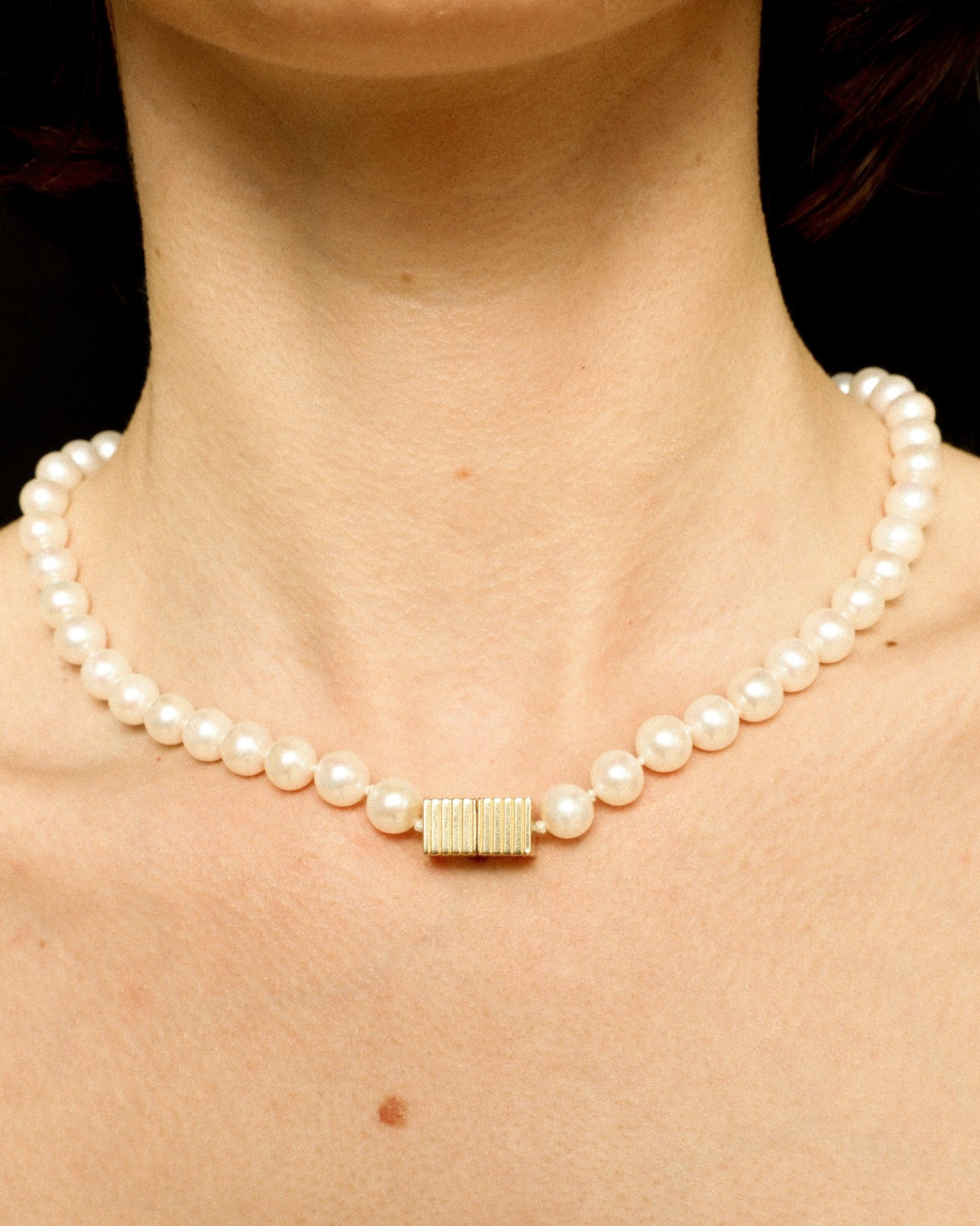 Pearl necklace with a gold clasp on a person's neck against a dark background