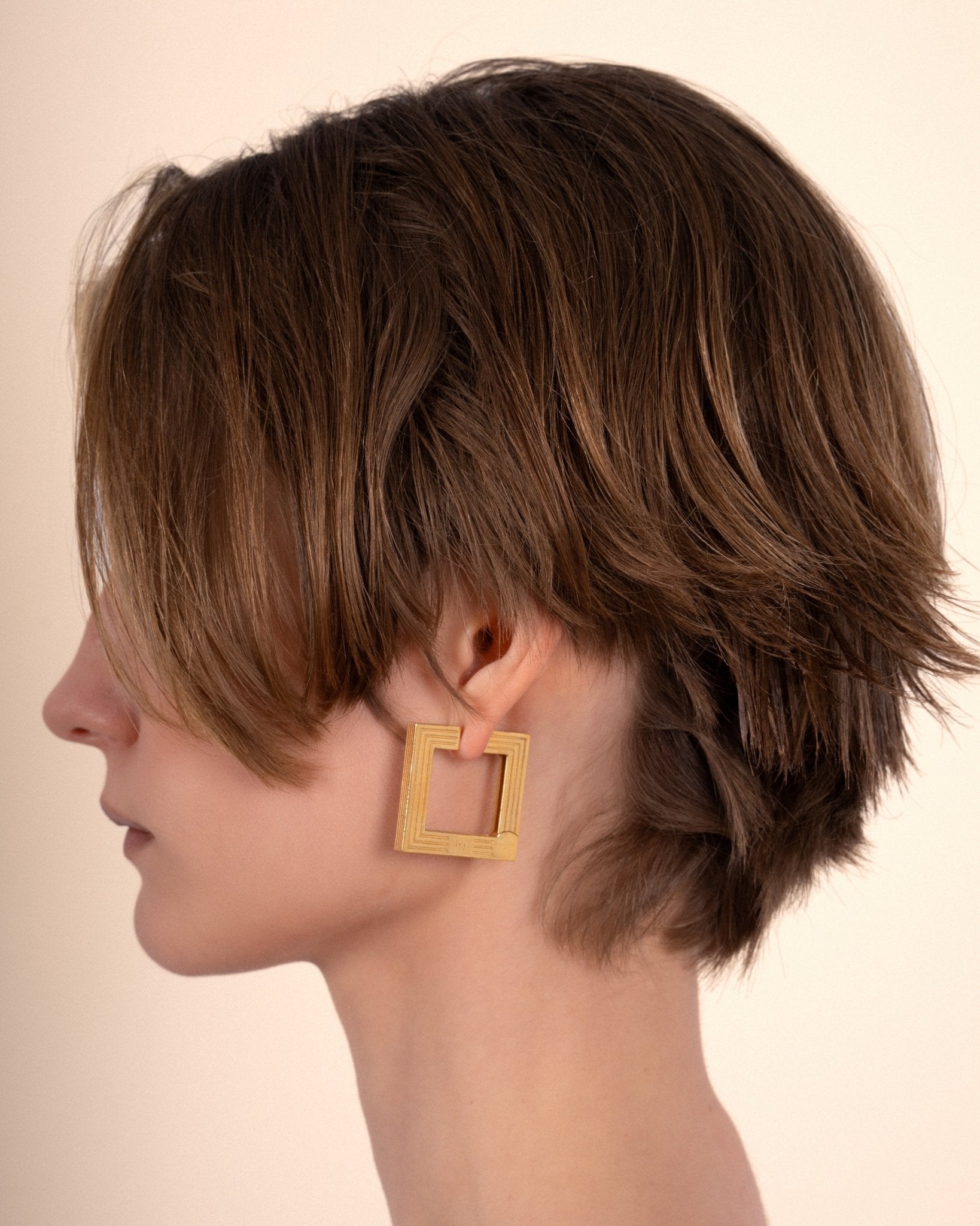 Large gold-plated sculptural hoop earrings worn by a model. 