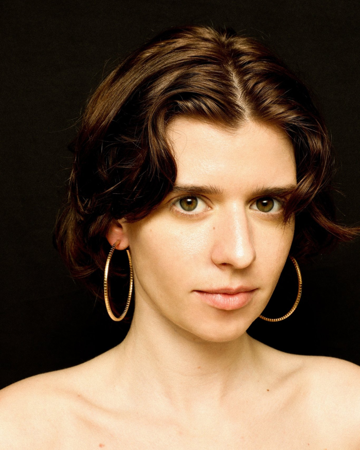 A pair of gold-plated Signore hoop earrings with a textured design, resembling a curving row of square beads worn by a model. 
