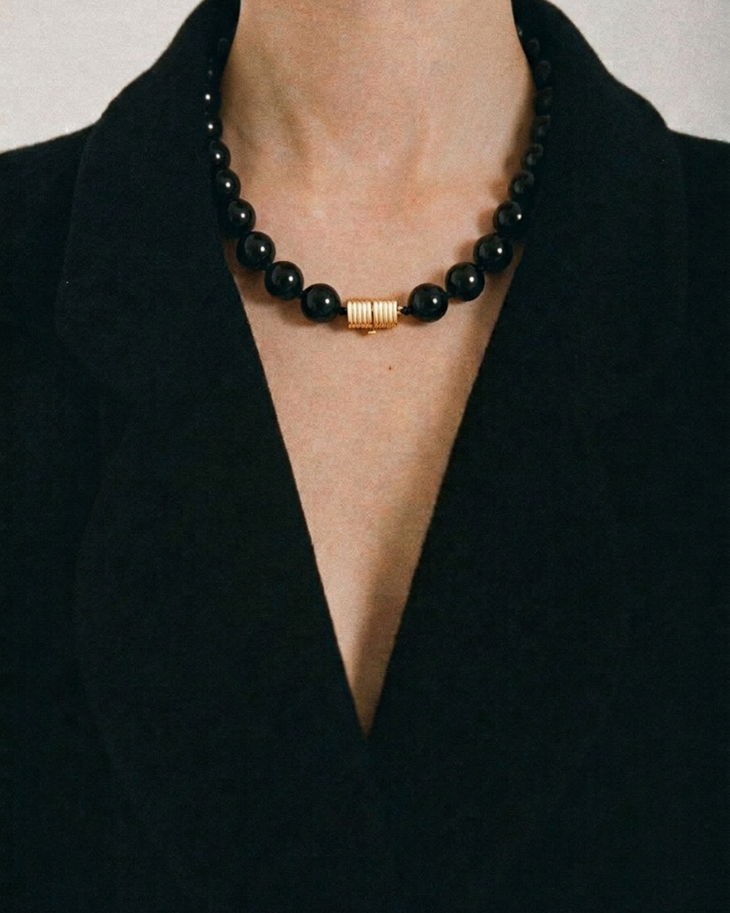 Black beaded necklace with a gold clasp worn by a person in a black outfit.