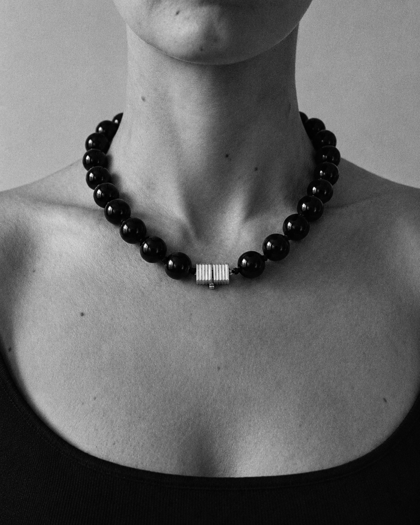 Black onyx beaded necklace with a gold clasp on a person wearing a black top against a neutral background