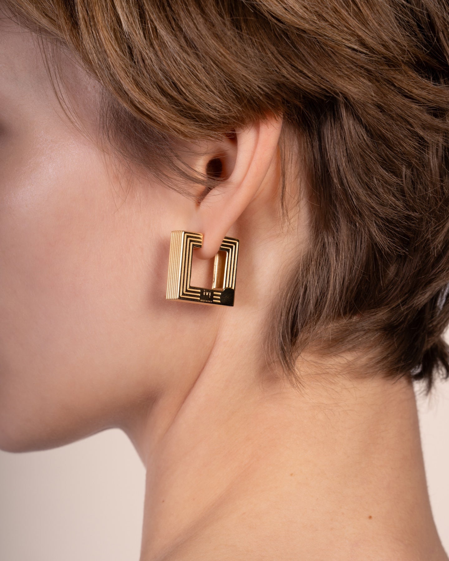 Pair of gold-plated medium Aurelia sculptural square hoop earrings worn by a model. 