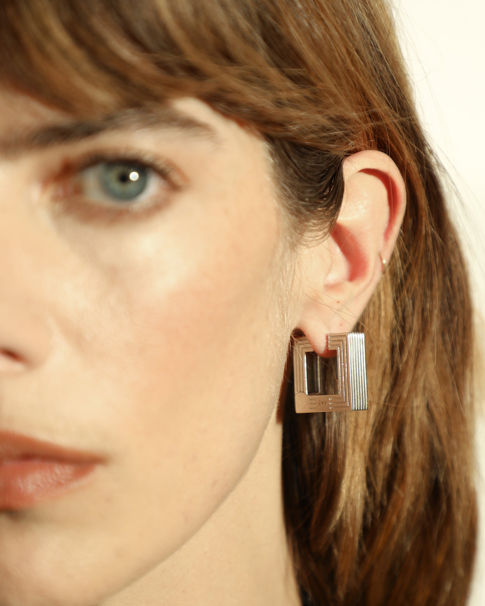 Pair of rhodium-plated medium Aurelia sculptural square hoop earrings worn by a model. 