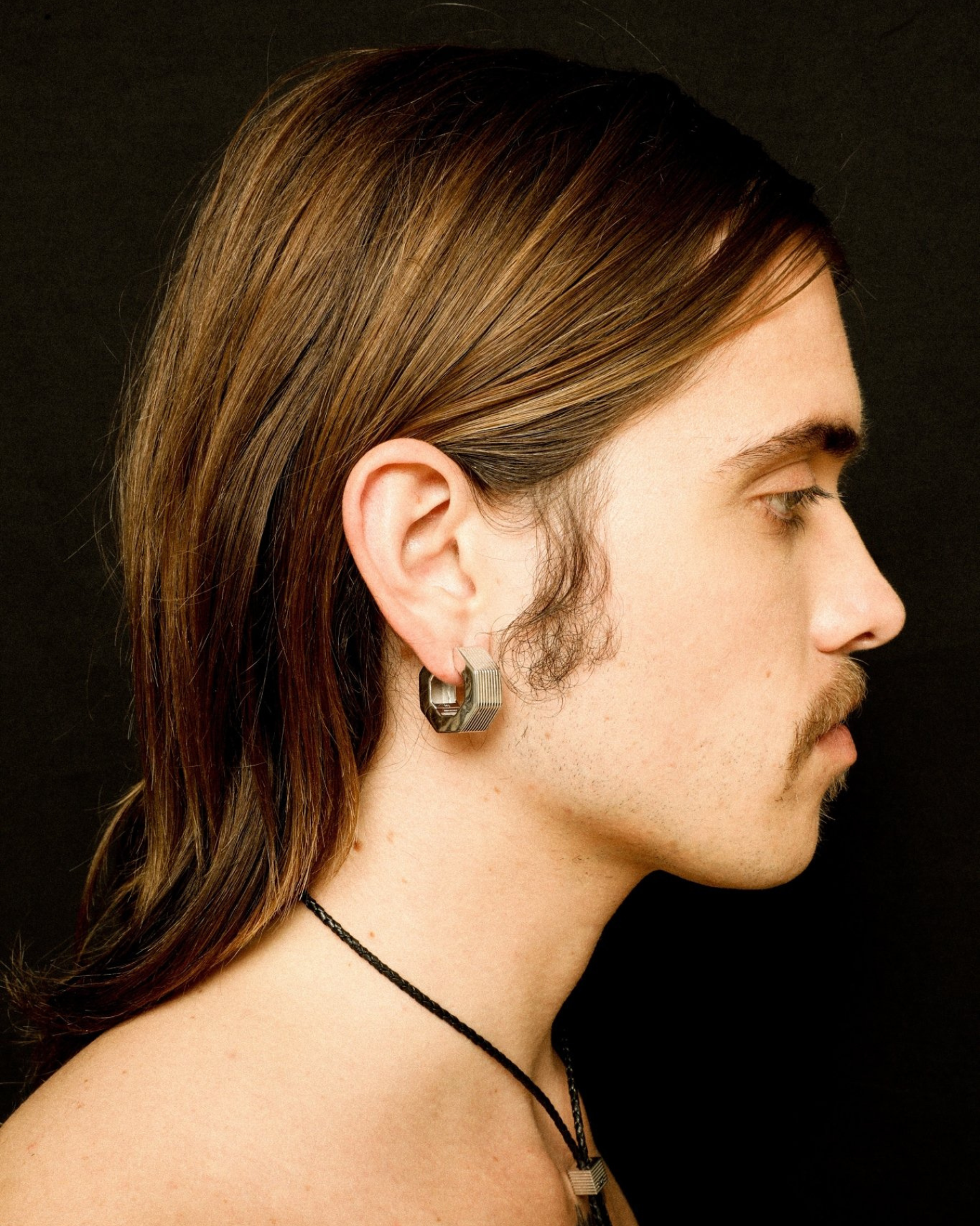 A pair of rhodium-plated medium-sized octagon hoop earrings with linear engravings worn by a model. 