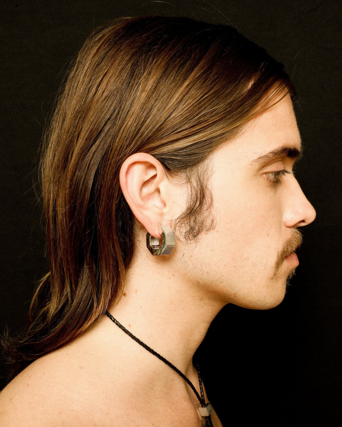 A pair of rhodium-plated medium-sized octagon hoop earrings with linear engravings worn by a model. 