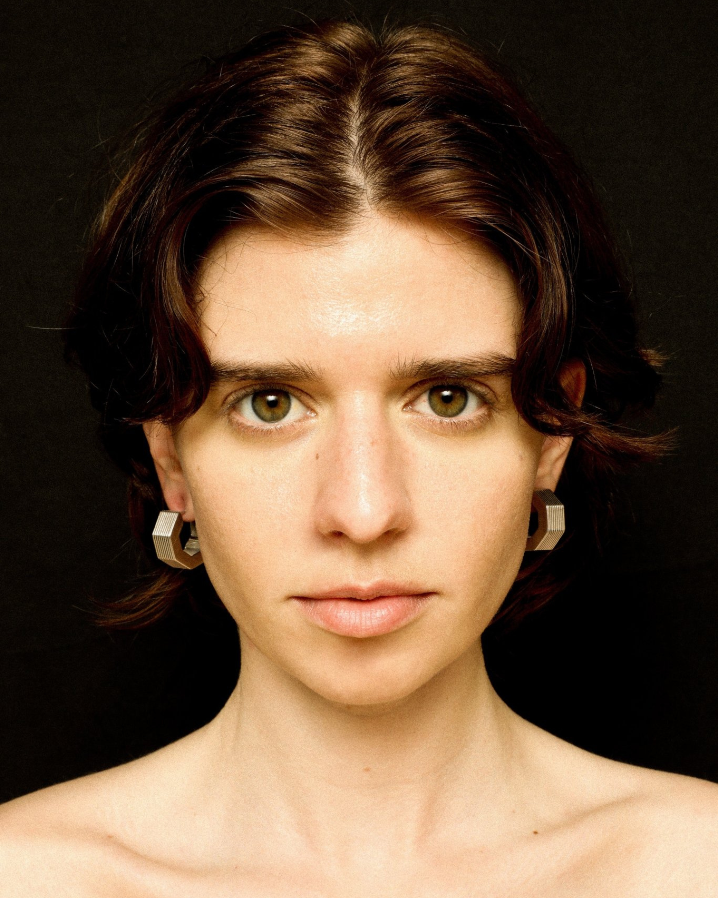 A pair of rhodium-plated medium-sized octagon hoop earrings with linear engravings worn by a model. 