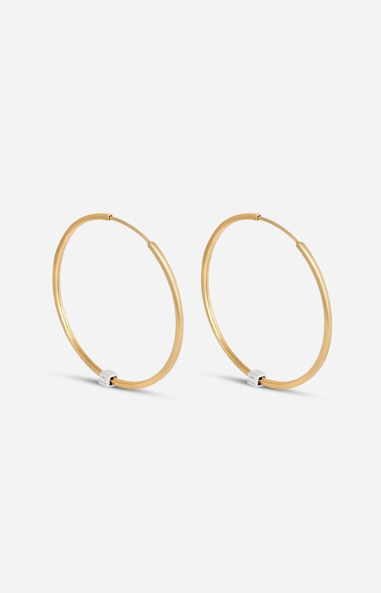A pair of gold-plated medium-sized hoop earrings with a single engraved cube detail on one side.