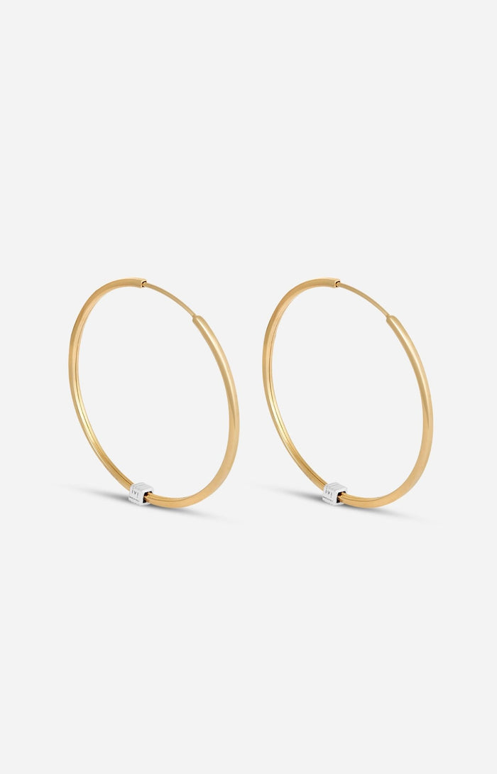 A pair of gold-plated medium-sized hoop earrings with a single engraved cube detail on one side.