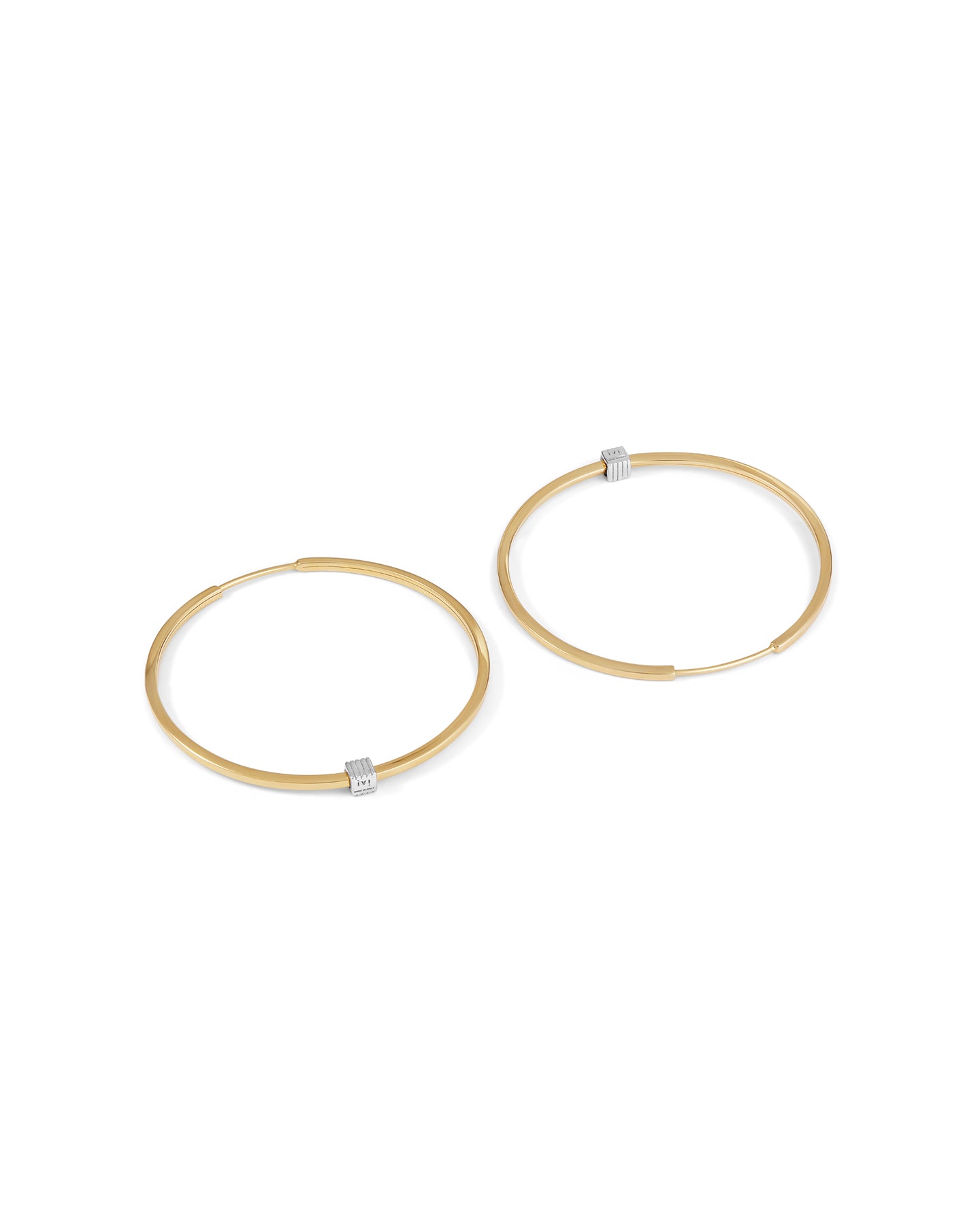 A pair of gold-plated medium-sized hoop earrings with a single engraved cube detail on one side.