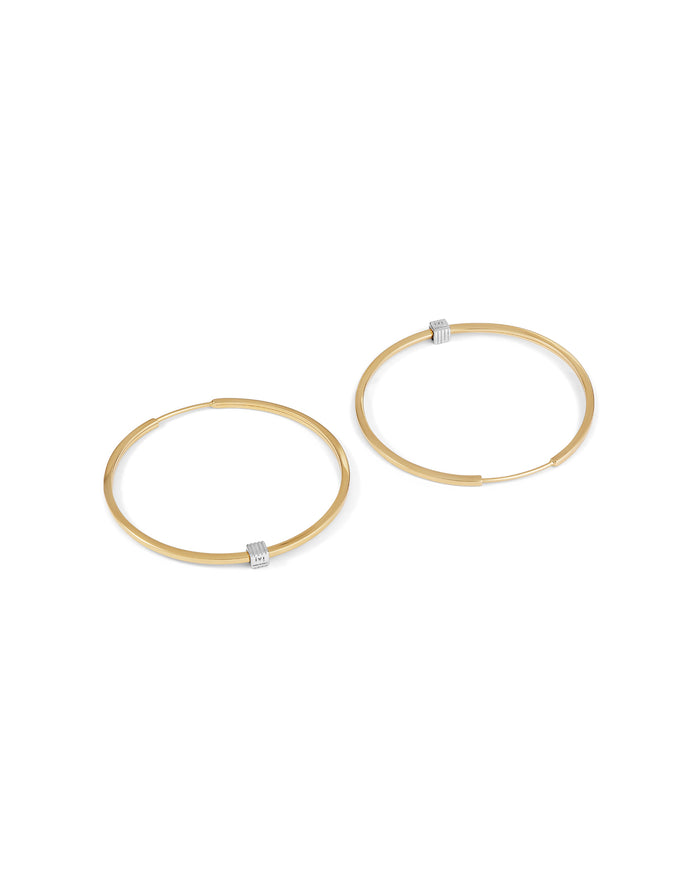 A pair of gold-plated medium-sized hoop earrings with a single engraved cube detail on one side.