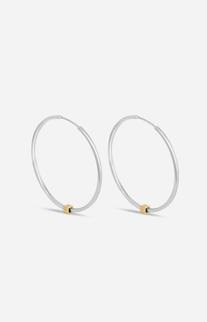 A pair of rhodium-plated medium-sized hoop earrings with a single engraved cube detail on one side.